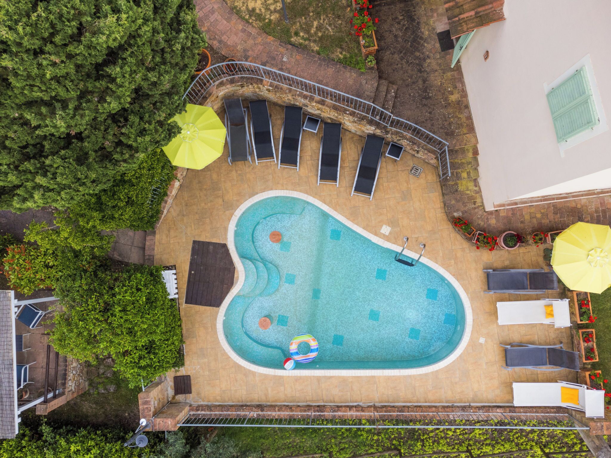 Eine Vogelperspektive zeigt einen Pool mit gewölbter Kante, umgeben von Liegestühlen und Sonnenschirmen.