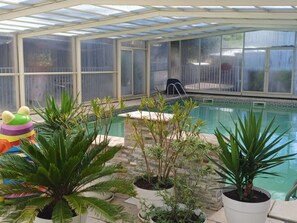 Un área de piscina interior con techo de vidrio, rodeada de plantas en macetas y un juguete inflable de colores.