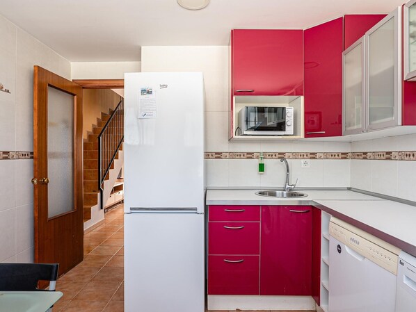 Una cocina compacta con refrigerador, microondas, pileta y muebles de color rojo.