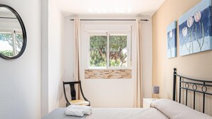 A bedroom with a bed, a chair, a window with curtains, and artwork on the wall.