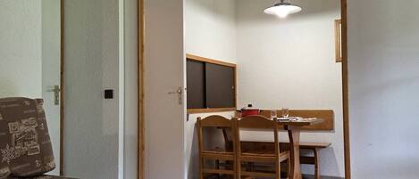 A compact room with a bed, a dining table with chairs, a ceiling light, and a door.