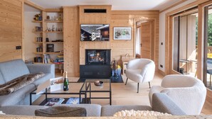 A modern living room with a fireplace, wooden walls, a sofa, a coffee table, and a TV mounted on the wall.
