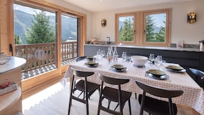 A dining area with a table set for four, large windows with mountain views, and a wooden deck.