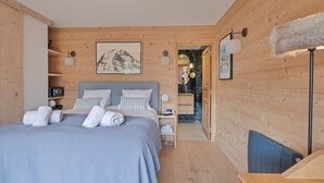 A modern bedroom with a large bed, wooden walls, and a view into the bathroom.
