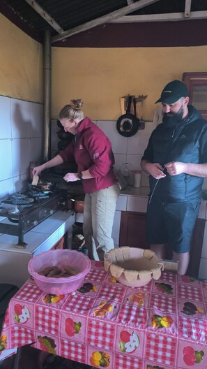 A kitchen with a gas stove, a woman cooking, and a man standing nearby. - Luquina 360 (Puno)