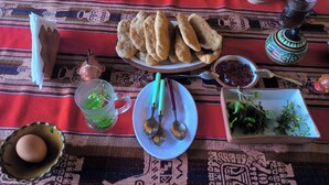 Une table avec une assiette de pain, une tasse de thé, un bol de confiture, une assiette d ’herbes aromatiques, un bol d’œufs et un pot décoratif.