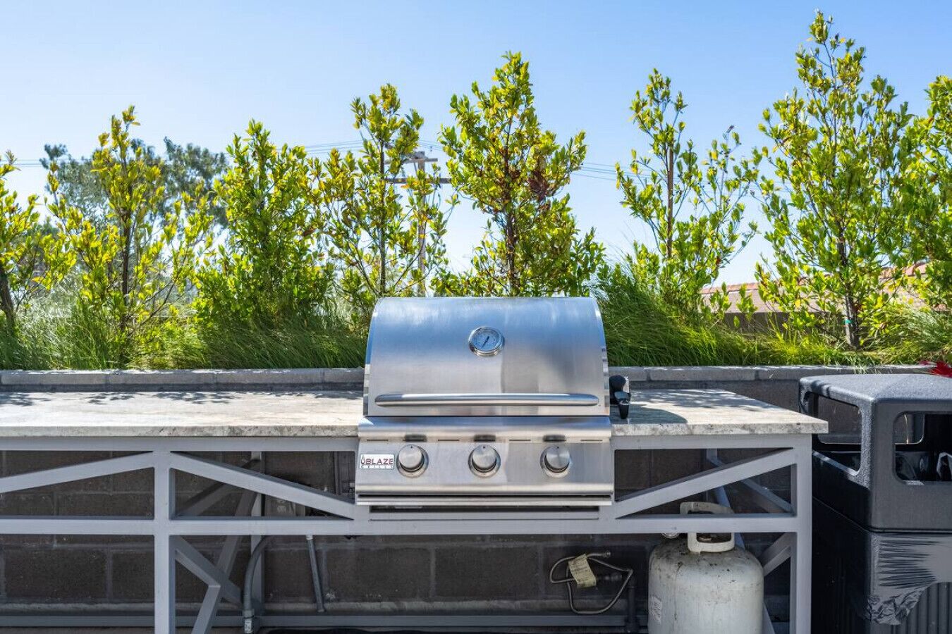 Ein Grill mit digitalem Thermometer auf einem Dach, zusammen mit einer Gasflasche und einer Grillabdeckung.