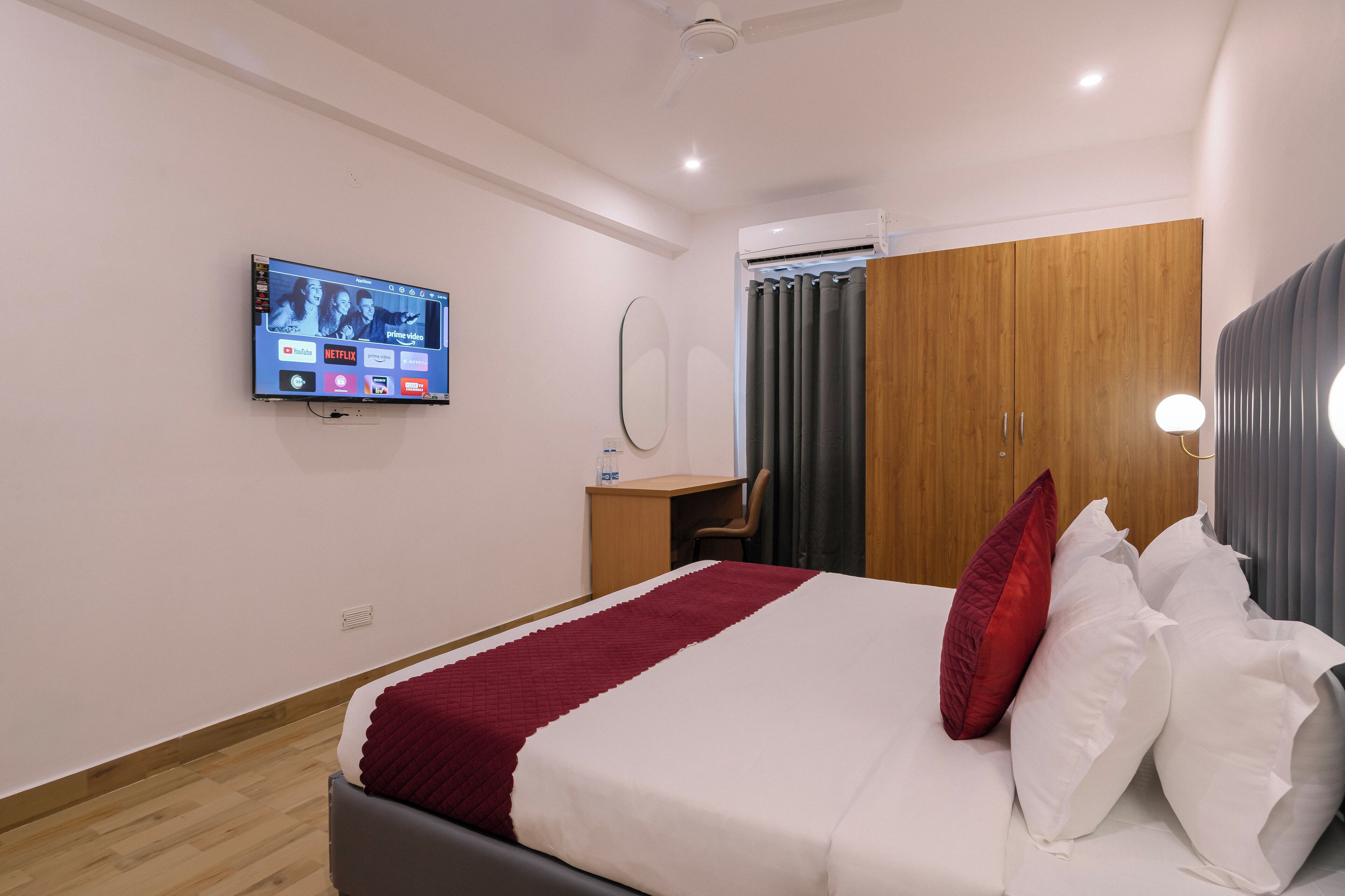 A hotel room with a bed, a desk, a television mounted on the wall, and a wardrobe.
