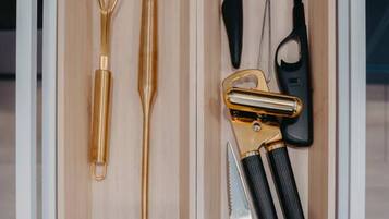 A kitchen drawer with a whisk, a slotted spoon, a ladle, a grater, and a pair of scissors.