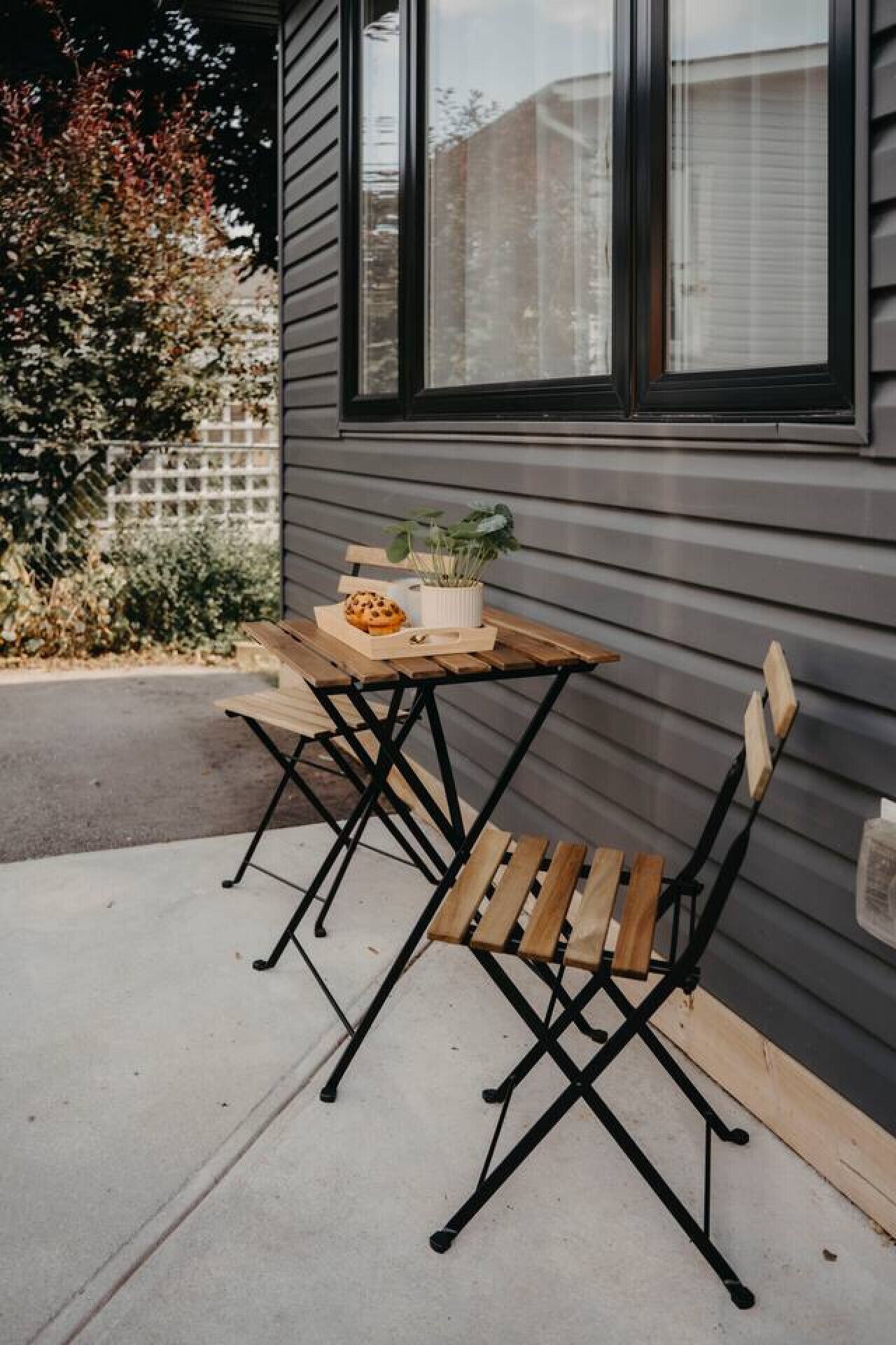 Une terrasse extérieure avec une table en bois et deux chaises, un pot de fleurs et une fenêtre avec des stores.