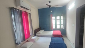 A hotel room with two beds, a ceiling fan, an air conditioning unit, and a window with curtains. - Marari beach daze homestay (Alappuzha)