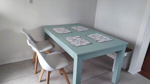 Een kleine eettafel met vier stoelen, een lichtblauwe tafelkleed en aan elke kant een tafelonderzetter met bloemen.