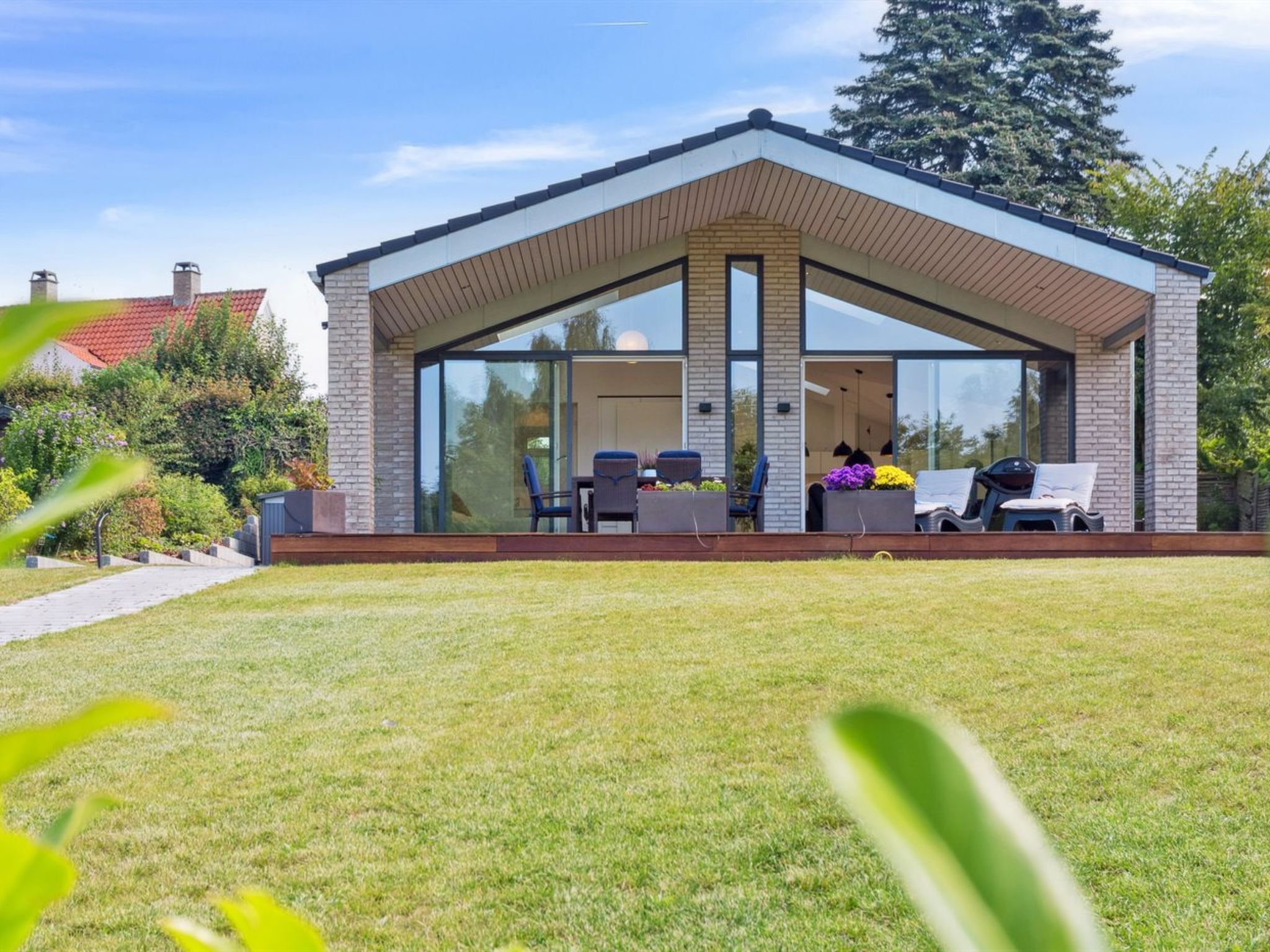 Una casa moderna con porche cubierto, ventanas amplias y mobiliario exterior.