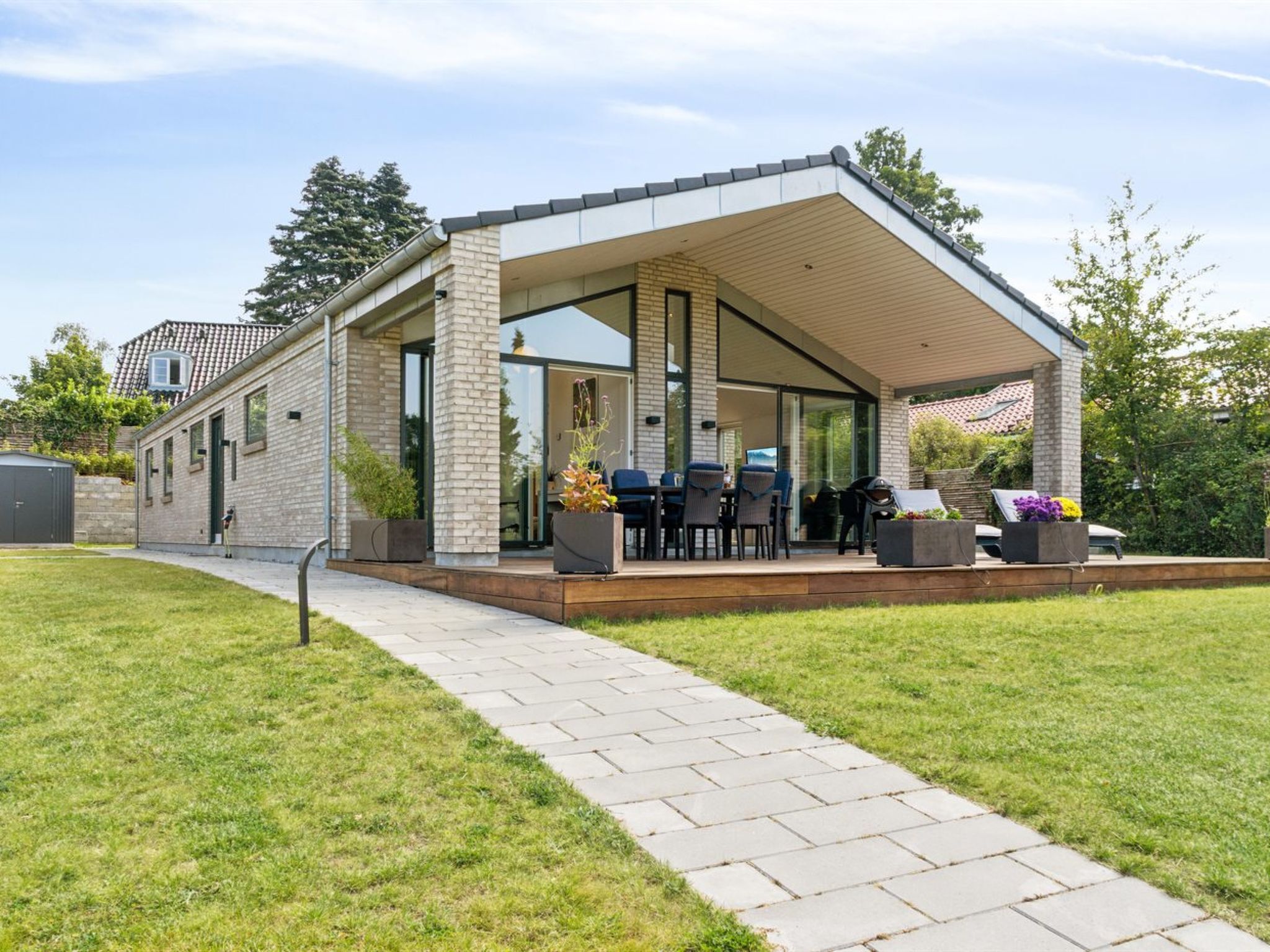 Una casa moderna con un porche cubierto, un sendero pavimentado y mobiliario exterior.