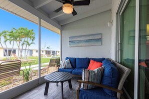 A covered patio with a sofa, a small table, and a ceiling fan.