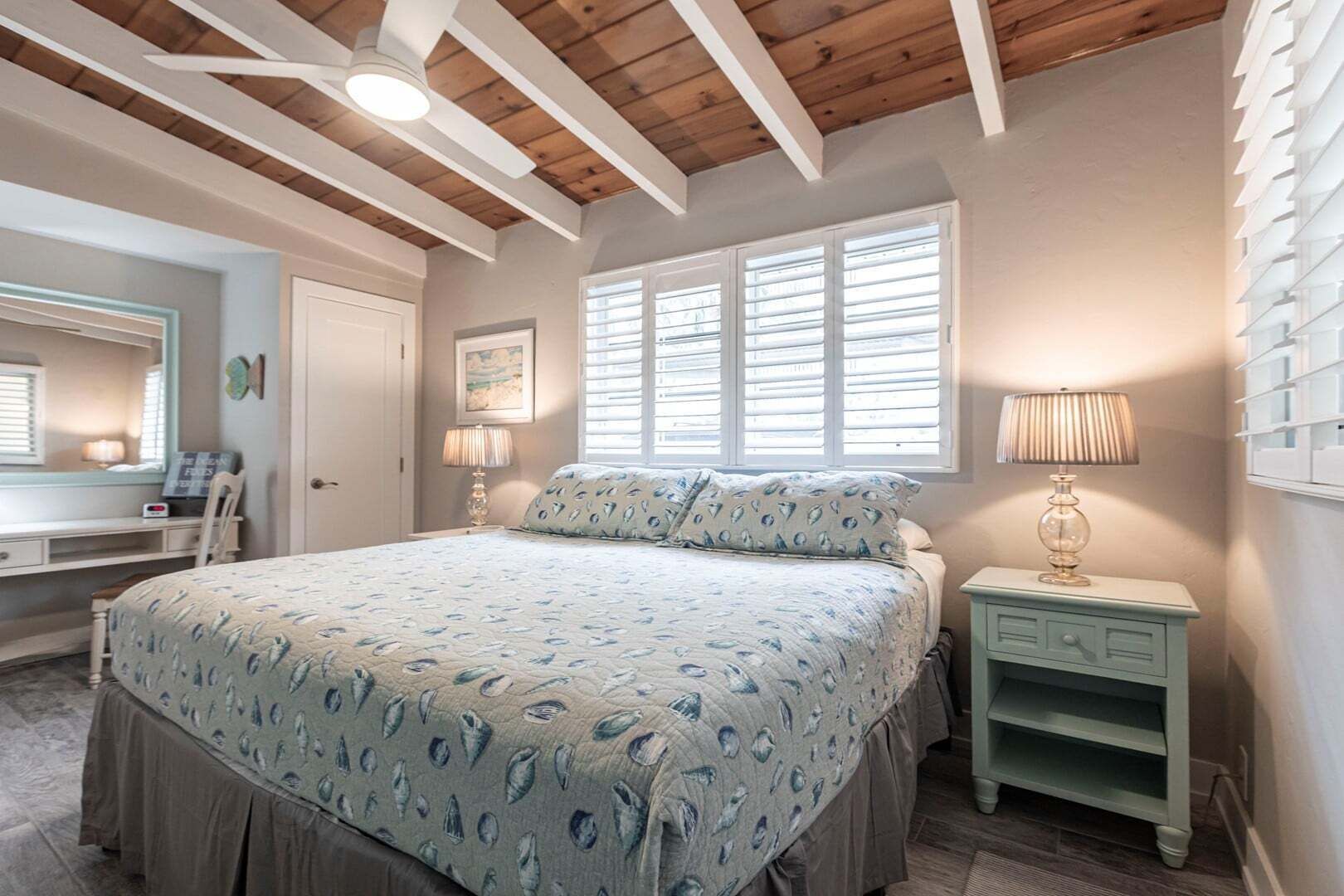 A bedroom with a bed, bedside tables, a desk, and a window with blinds.