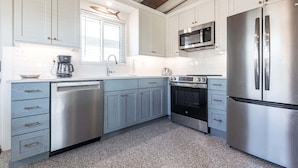 Una cocina moderna con electrodomésticos de acero inoxidable, muebles de cocina blancos y techo de madera.
