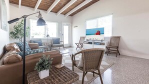 Amplia sala de estar con sofá, sillas, televisión y un ventanal con vista a la playa.