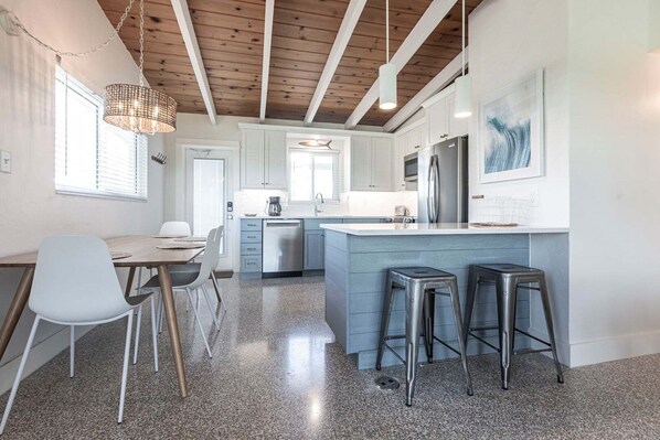 A modern kitchen with a central island, bar stools, and a dining area with chairs.