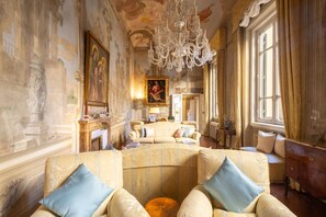 Ein luxuriöses Zimmer mit aufwendiger Dekoration, darunter eine große Chandelier, klassische Gemälde und komfortable Sitzmöglichkeiten.