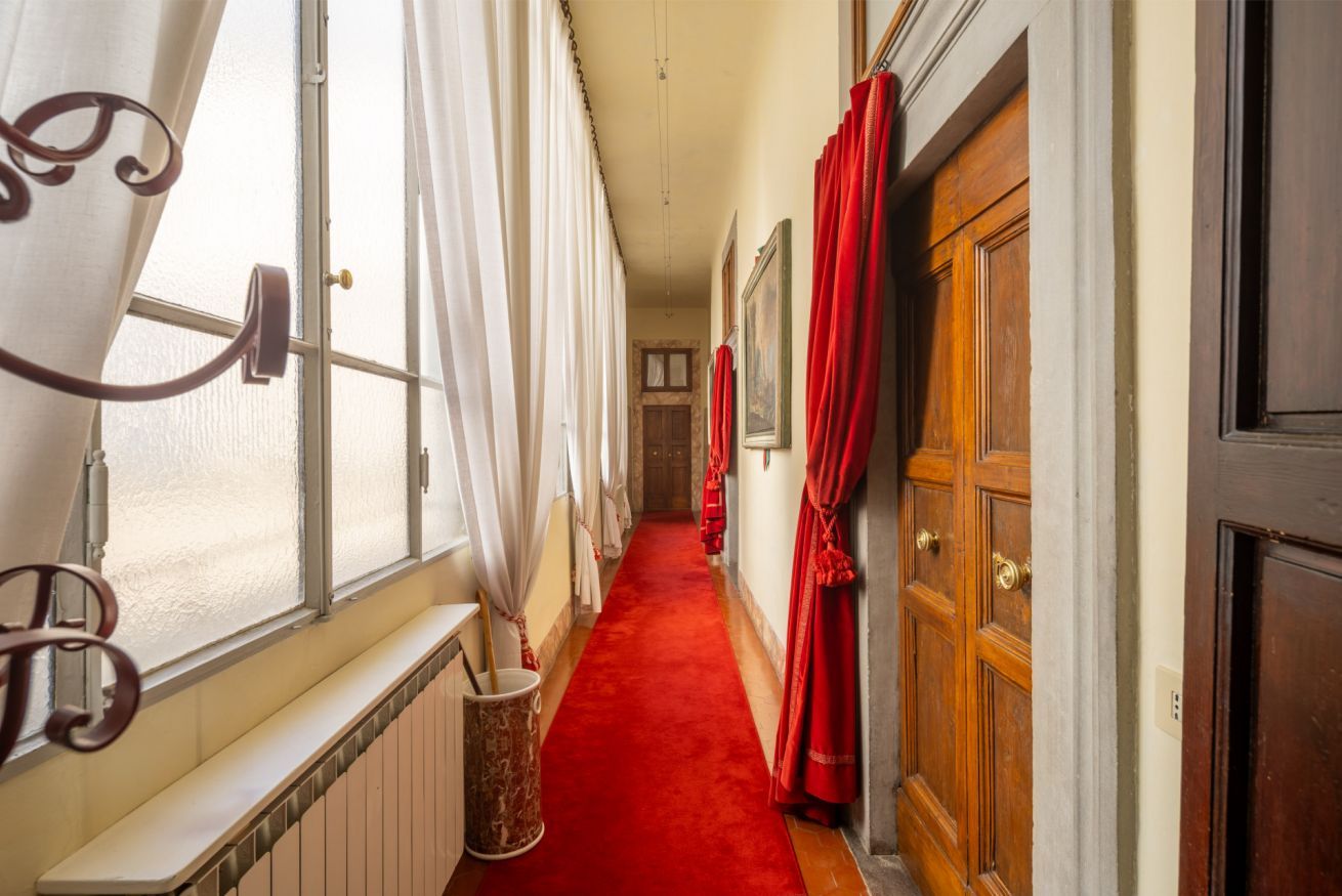 A corridor with a red carpet, wooden doors, and white curtains.
