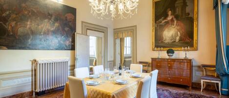 A dining room with a large table set for six, a chandelier, a large painting, and a classic wooden dresser.