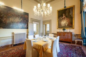 A dining room with a large table set for six, a chandelier, a large painting, and a classic wooden dresser.