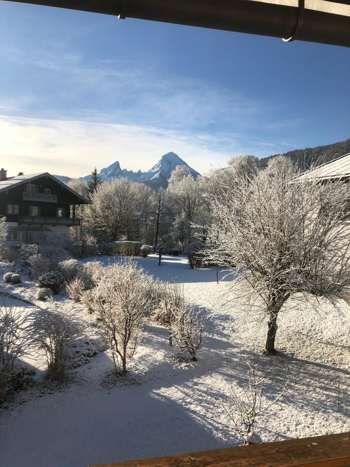 A snow-covered landscape with a mountain in the background, a wooden building, and a clear sky.