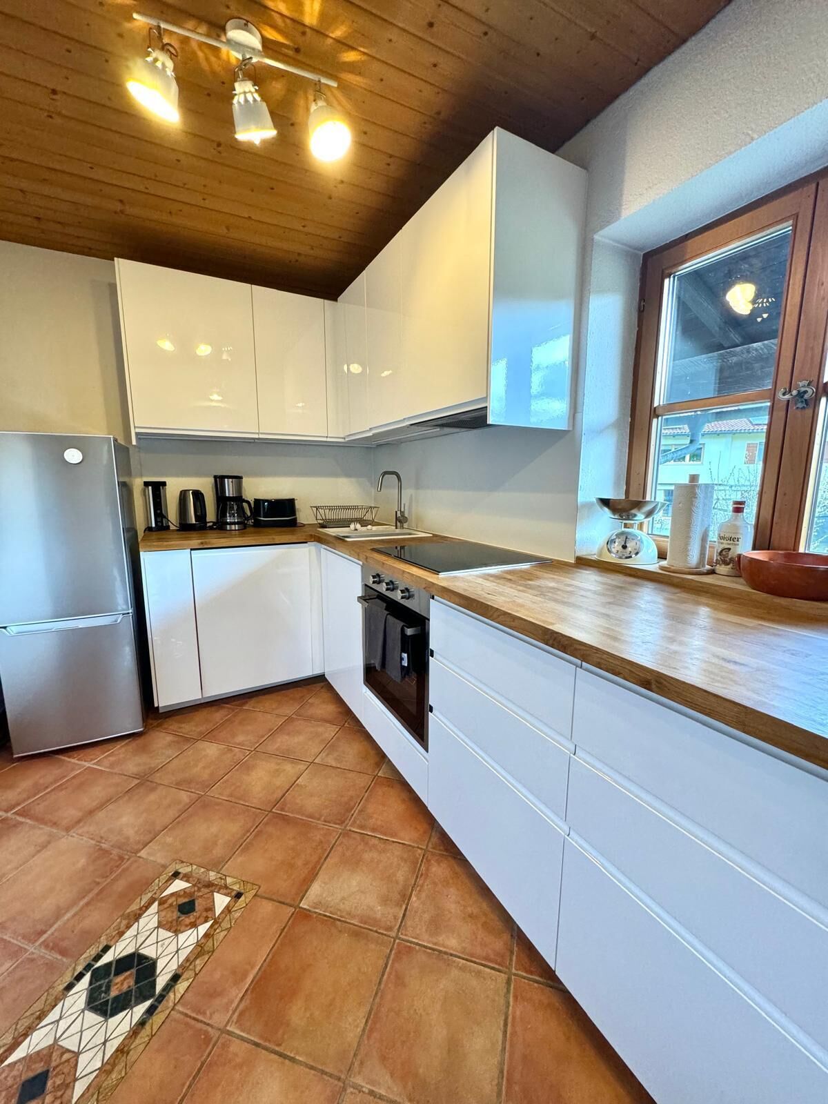 A modern kitchen with white cabinets, a stainless steel refrigerator, a built-in oven, and a wooden countertop.