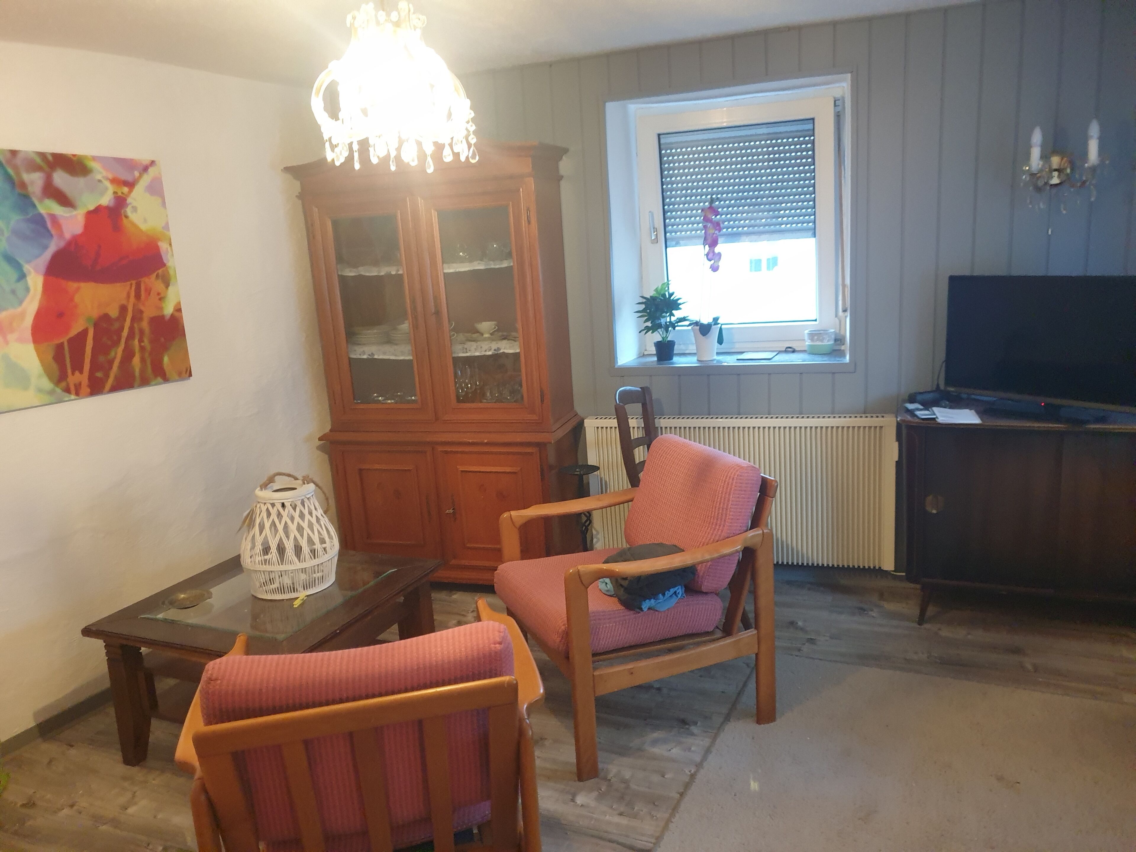 A living room with a wooden cabinet, a television, and a window with blinds.
