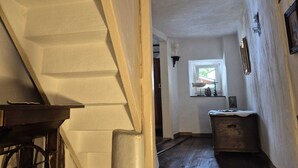 Un pasillo estrecho con suelo de madera, una ventana con vistas y una pequeña mesa con una silla.