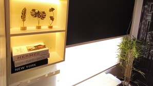 Une chambre moderne avec une étagère intégrée où sont exposés des livres et des objets décoratifs, une grande fenêtre et une plante en pot.