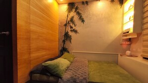 Une petite pièce comprenant un lit, une petite étagère à livres et une étagère murale où sont disposés des objets décoratifs.