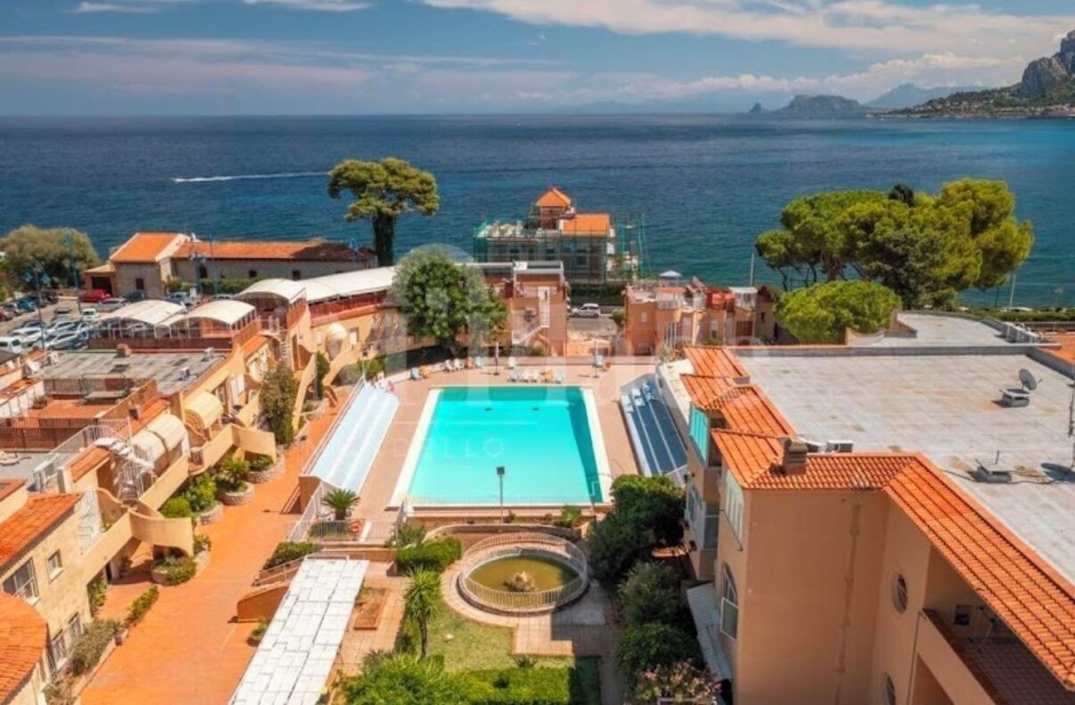 A hotel with a swimming pool, terraced balconies, and a view of the sea.