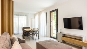 Un salon moderne comprenant un canapé, un pouf, une table à manger, des chaises et un téléviseur à écran plat fixé au mur.