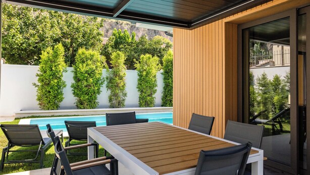 Une terrasse extérieure avec une piscine, entourée de verdure et d’un mur en bois.