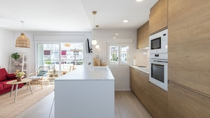 A modern kitchen with a central island, wooden cabinets, and built-in appliances. - Exclusive Seaside Living - Modern Comfort - Steps from the Beach (Cambrils)
