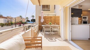 A balcony with a wooden bench, a table with chairs, a TV, and a kitchen area with cabinets and appliances. - Exclusive Seaside Living - Modern Comfort - Steps from the Beach (Cambrils)
