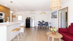 A modern kitchen with a microwave, stove, and sink. There is a dining area with a table and chairs, and a red sofa in the living room. - Exclusive Seaside Living - Modern Comfort - Steps from the Beach (Cambrils)