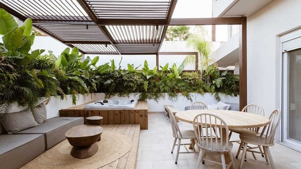 Eine Terrasse mit Holztisch und Stühlen, einem Whirlpool und einer Sitzecke mit Sofa und Kissen.