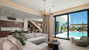 A modern living room with a large sofa, a coffee table, and a view of a swimming pool. - Lanik Luxury Pool Villa (Αφάντου)
