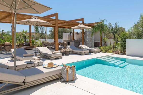 A poolside area with lounge chairs, umbrellas, and a stone wall.