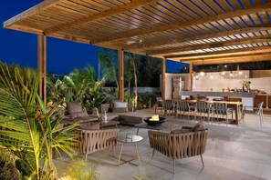 An outdoor patio with a wooden pergola, seating area, and a kitchen.