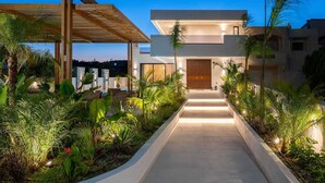 A modern house with a wooden pergola, a paved pathway, and tropical plants. - Lanik Luxury Pool Villa (Αφάντου)