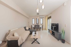 A modern living room with a sofa, coffee table, TV, and dining area.