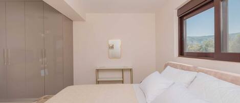 A bedroom with a bed, a wardrobe, a bedside table, a mirror, and a window with a view.