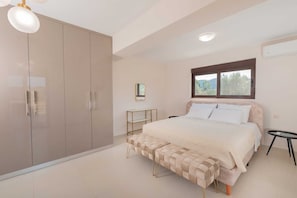 Un dormitorio con cama, armario, banca, mesita de noche y ventana.