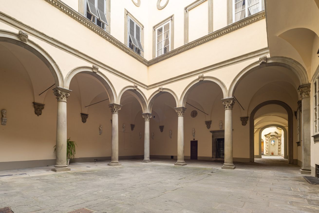 Une vaste cour intérieure, agrémentée de nombreuses arcades et de colonnes, qui mène à une porte située au loin.