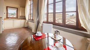 A dining area with a table set for two, a window with curtains, and a view of a cityscape. - Tower View Apartment (Firenze)