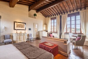 A hotel room with a bed, a sofa, a dining table, and a view of the city.